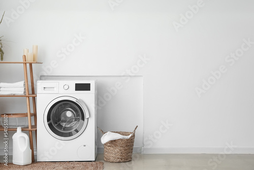 Interior of light laundry room with washing machine, basket and shelving unit photo