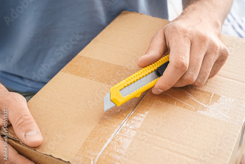 Man with cardboard box and utility knife, closeup photo