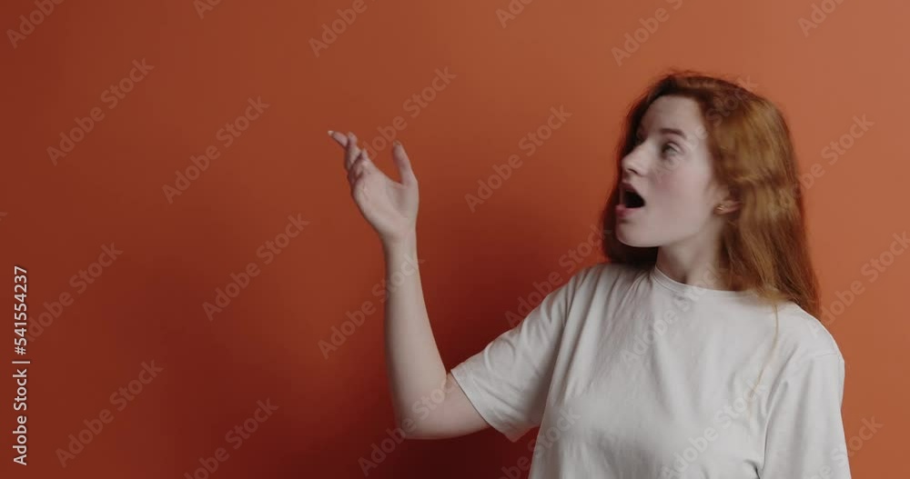 Surprised woman pointing aside. Amused young ginger girl points fingers away Surprised woman pointing aside. Amused young ginger girl points fingers away
