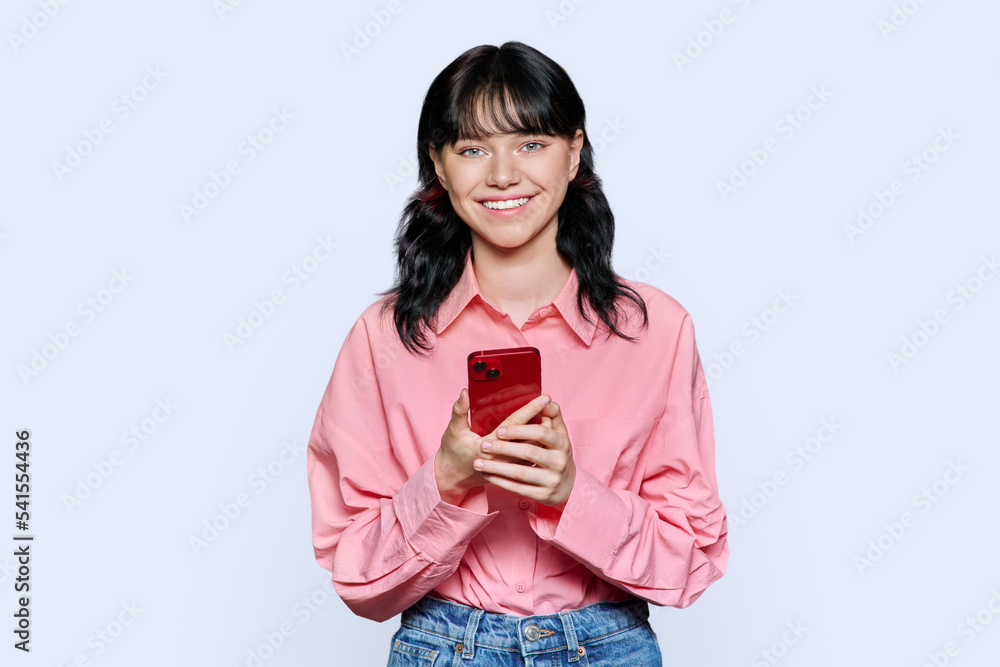 Young teenage girl with smartphone looking at camera on light background Young teenage girl with smartphone looking at camera on light background