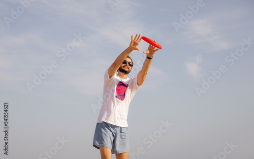 Man catches Frisbee with a smile on his face. Game of Frisbee. Beach activities. Time for relaxation. Summer entertainment