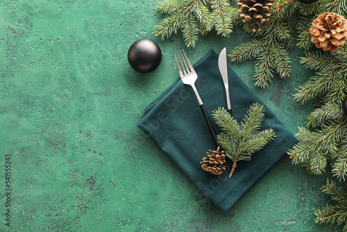 Napkin with cutlery  Christmas ball  fir branches and cones on green background