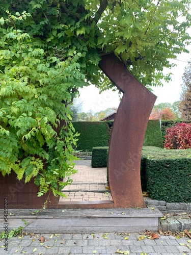 Rusty metal in the garden. Beautiful Corten steel arch entwined with Campsis radicans leaves in the autumn garden. Appeltern, Netherlands, October 12, 2022  photo