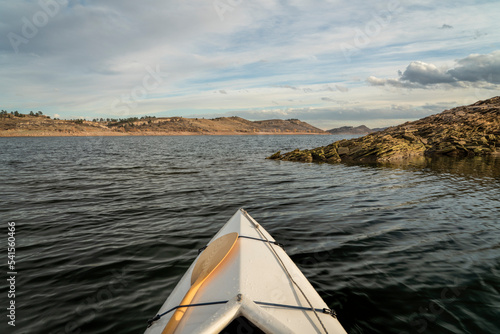 bow of a decked expedition canoe with wooden paddle on a mountain lake, paddler view - Horsetooth Reservoir in northern Colorado