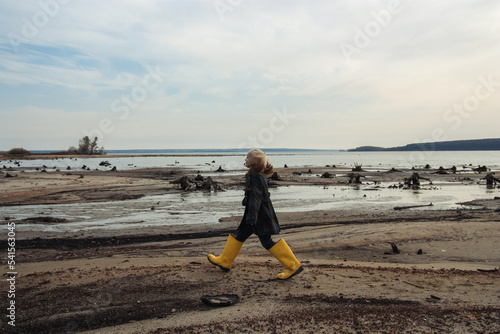 girl in big yellow rubber boots walking at seashore