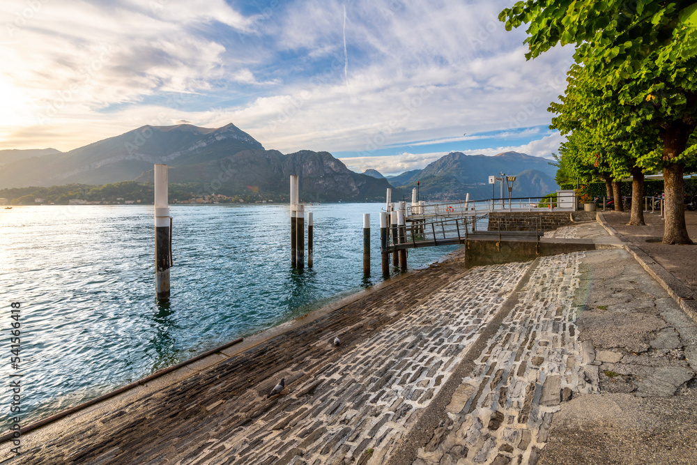 View from the waterfront promenade of the mountains and Lake Como, with boats and ferries at the port of the village of Bellagio, Italy.
