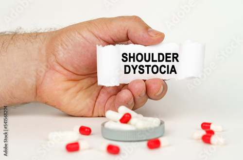 On a white background, medical capsules, in the hands of a person a paper plate with the inscription - Shoulder dystocia photo