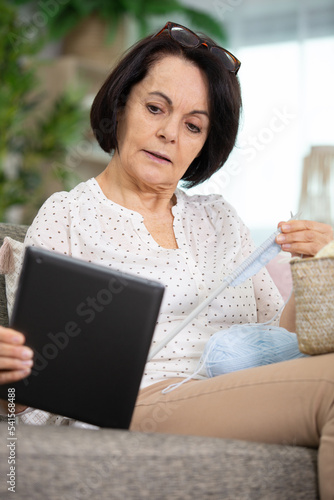 senior-woman sitting on sofa with yarn and needles and tablet