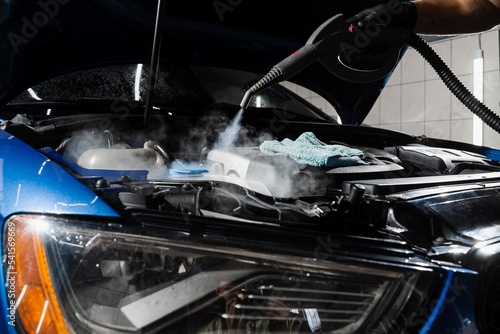 Steaming washing of motor of auto in detailing auto service. Process of steam cleaning car engine from dust and dirt.