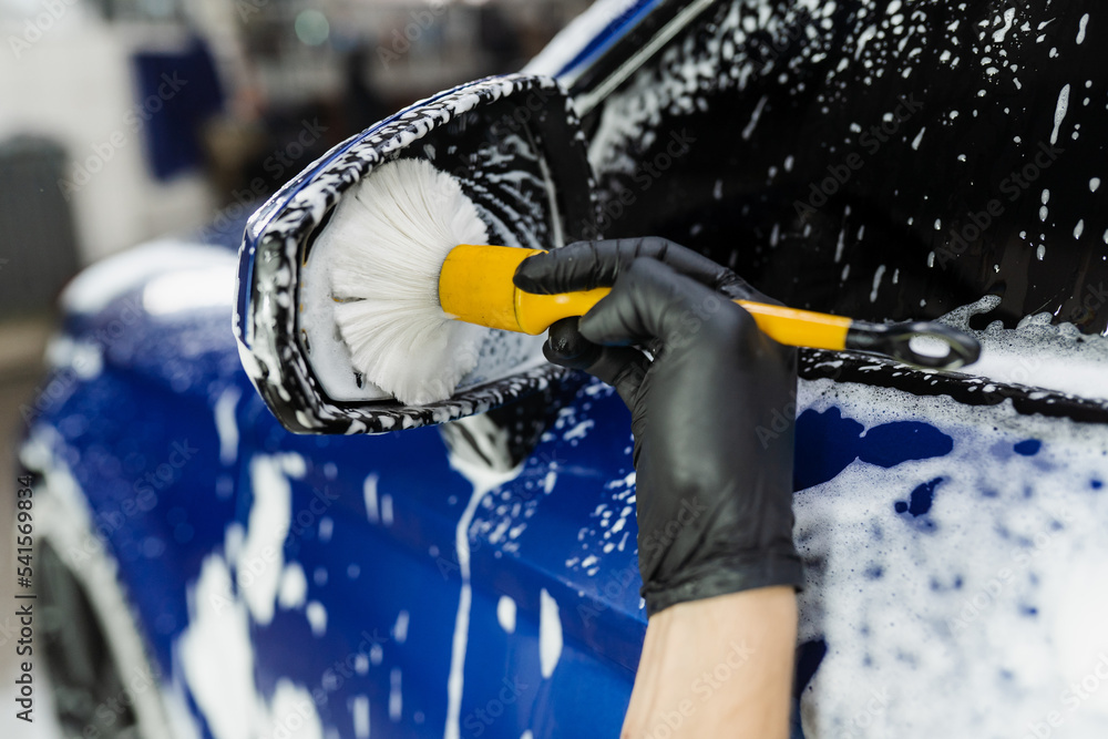 Hand brush washing of car side mirror with foam in car detailing