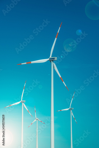 Big wind turbines to generate electrical power as green energy at blue turquoise sky, direct sunlight illumination with lens flare and copy space © neurobite