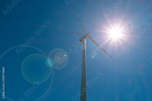 Big wind turbine to generate electrical power as green ecofriendly energy at blue deep sky, direct sunlight illumination with lens flare and copy space. © neurobite
