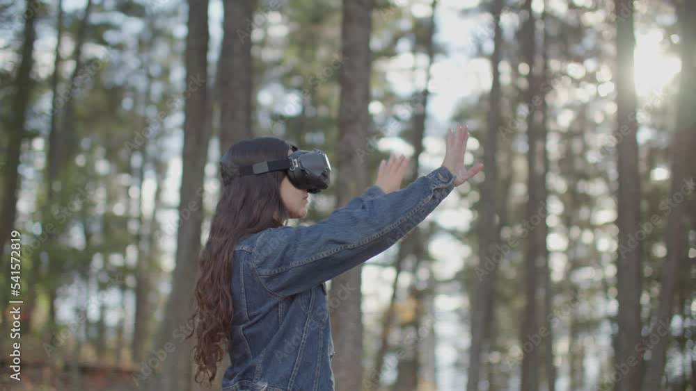 Young woman wearing vr goggles using virtual reality interface in beautiful forest Young woman wearing vr goggles using virtual reality interface in beautiful forest
