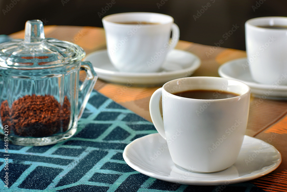 table with three cups of black coffee on a dark background. Orange and blue tablecloth table with three cups of black coffee on a dark background. Orange and blue tablecloth