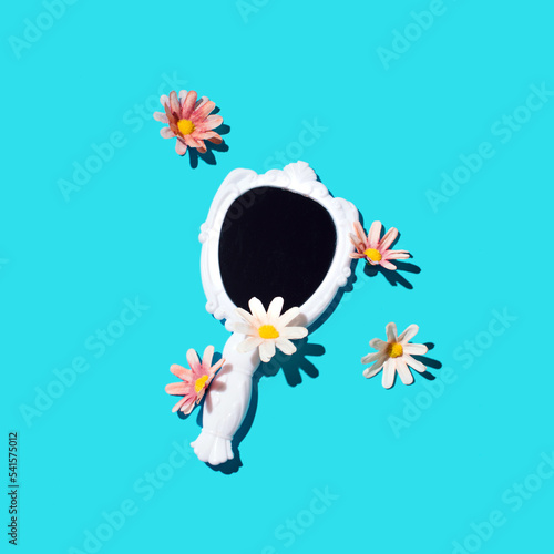 Hand mirror decorated with daisy flowers, creative beauty concept, bright blue background.  photo