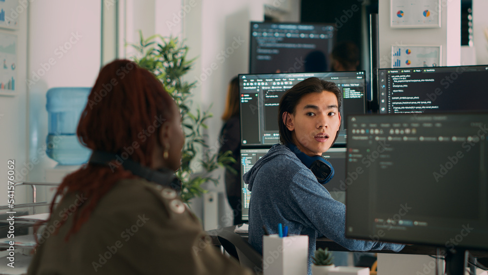 Asian system engineer asking coder for help with html code, pointing at database script on terminal window. Team of diverse developers working on app developing program in data room. Asian system engineer asking coder for help with html code, pointing at database script on terminal window. Team of diverse developers working on app developing program in data room.