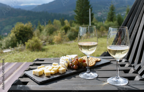 Two glasses of white wine and plate of cheese and grapes on table outdoor