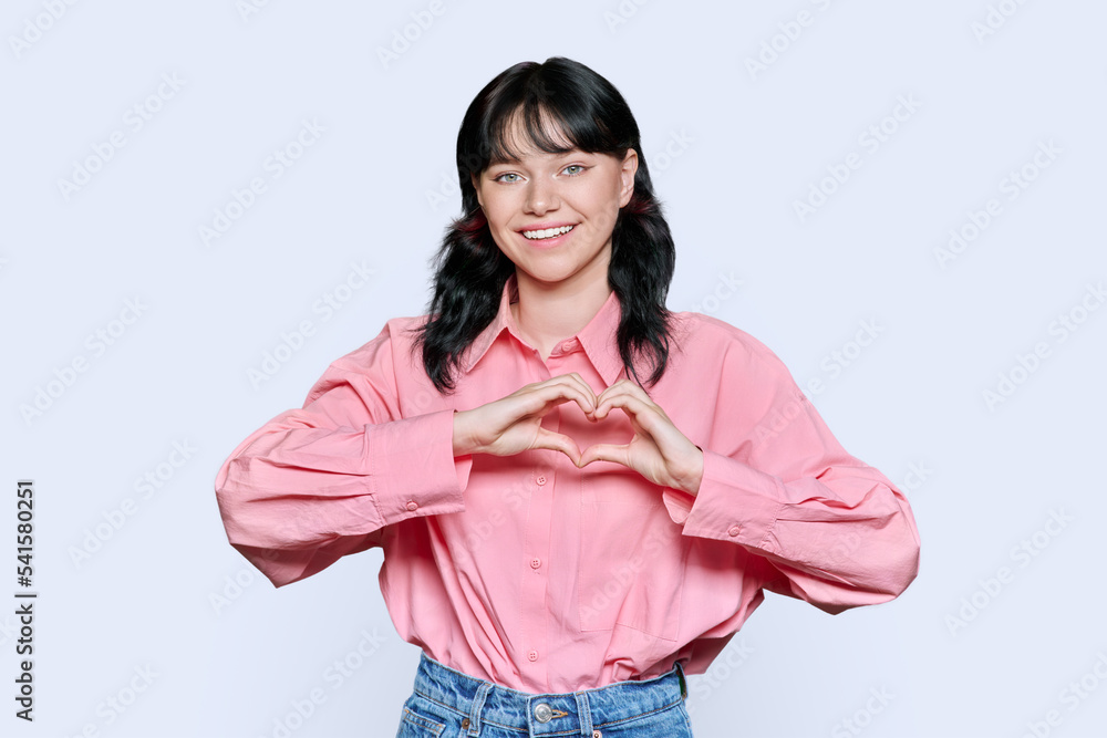Young smiling female showing heart gesture with fingers, white background Young smiling female showing heart gesture with fingers, white background