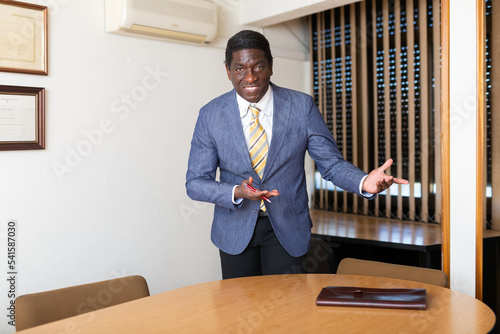 Friendly businessman invites to sit down at the negotiating table in modern office