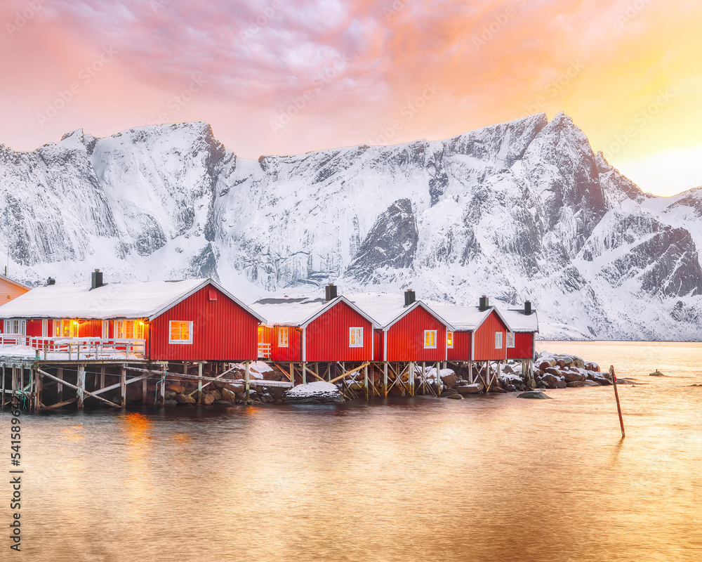 Fototapeta premium Traditional Norwegian red wooden houses (rorbuer) on the shore of Reinefjorden near Hamnoy village at sunset.
