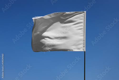 White flag fluttering against blue sky on sunny day