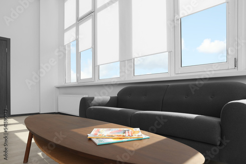 Obraz na płótnie Comfortable sofa and table near large window with white roller blinds indoors