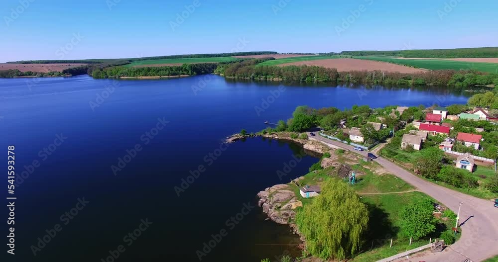 Automobile road with some cars at the waterfront. Drone flying over the azure river on sunny day. Agricultural fields at backdrop. Automobile road with some cars at the waterfront. Drone flying over the azure river on sunny day. Agricultural fields at backdrop.