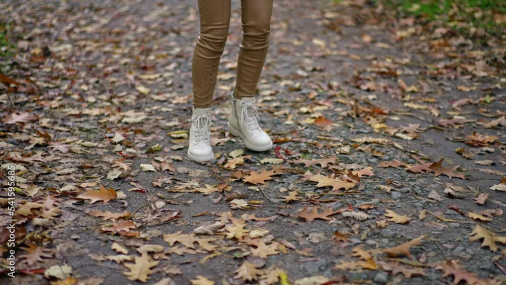 Unrecognized lady in beige pants and white jacket and boots walking in the park. Long-haired brunette turning around demonstrating her look. Unrecognized lady in beige pants and white jacket and boots walking in the park. Long-haired brunette turning around demonstrating her look.
