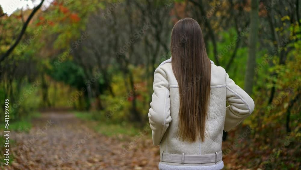 Following the lady with beautiful long dark hair walking in the park. Woman turns her head smiling to the camera. Autumn nature backdrop. Following the lady with beautiful long dark hair walking in the park. Woman turns her head smiling to the camera. Autumn nature backdrop.