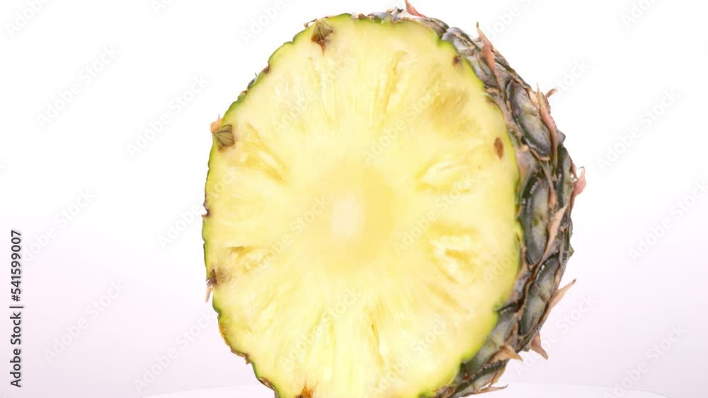 Front view of halved pineapple lying on a rotating table, white background. Front view of halved pineapple lying on a rotating table, white background.