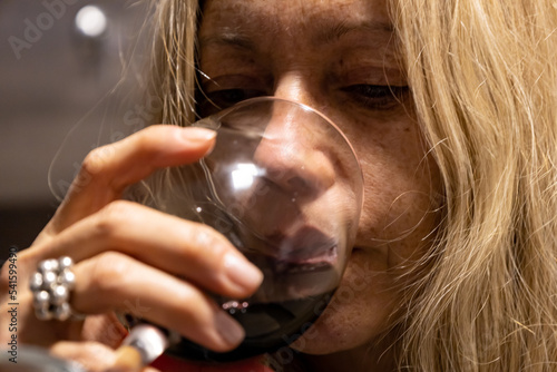 Young woman with blond hair drinking from a glass cup What contains red wine.
