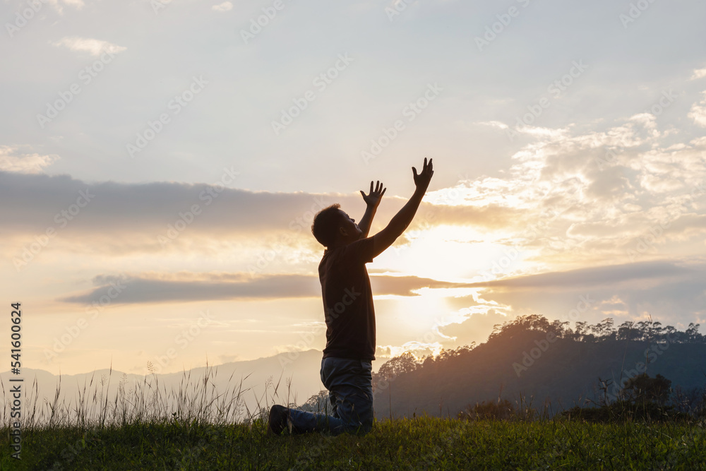 Young male kneeling down with hands open palm up praying to God on the mountain sunset background. Young male kneeling down with hands open palm up praying to God on the mountain sunset background.
