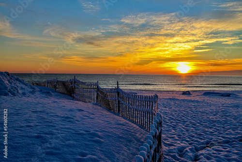 sunset or sunrise in the ocean, golden sky, beautiful sun, blue and white clouds, winter snow on the beaches sand