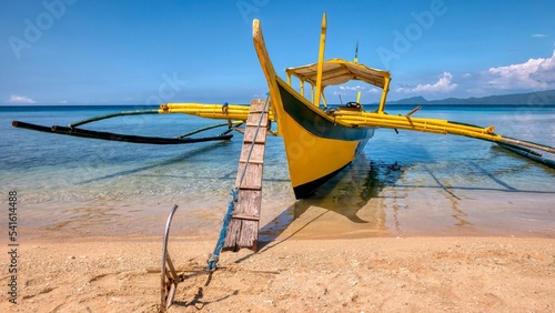 Closeup view of the bow of a wooden outrigger boat in the Philippines, locally known as a banca, anchored in shallow turquoise water, with its wooden gangplank and anchor on a tropical island beach.