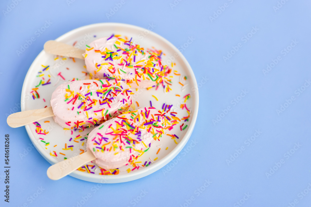 Bright and colorful flat lay of pink strawberry Popsicle ice cream with mint on blue background. Healthy summer food concept. Top view of popsicle with sprinkles, overhead Bright and colorful flat lay of pink strawberry Popsicle ice cream with mint on blue background. Healthy summer food concept. Top view of popsicle with sprinkles, overhead