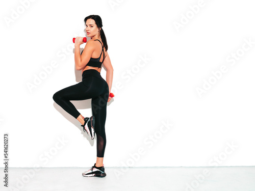 Fitness confident woman in black sports clothing. Sexy young beautiful model with perfect body. Female isolated on white wall in studio. Stretching out before training.Making exercises with dumbbells