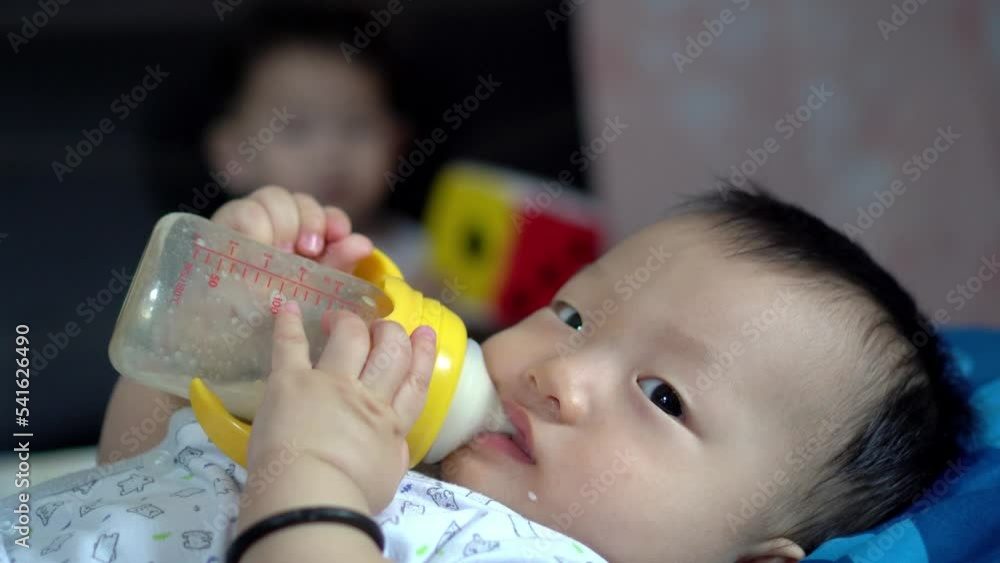 Baby boy drink milk. Elder brother play at the back Baby boy drink milk. Elder brother play at the back