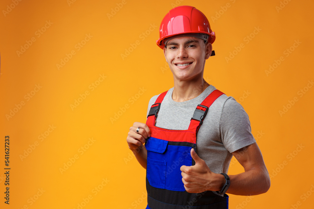 Young construction worker in helmet and uniform posing on yellow background in studio Young construction worker in helmet and uniform posing on yellow background in studio