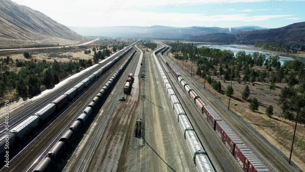 forward flight dolly drone shot flying over a railroad station in a desert environment on a sunny day next to a highway and a river and mountains in the background and powerines in the picture forward flight dolly drone shot flying over a railroad station in a desert environment on a sunny day next to a highway and a river and mountains in the background and powerines in the picture