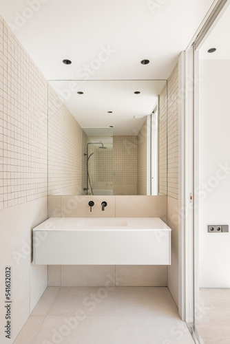 Modern bathroom with beige tiles. shower zone with glass partition reflected in the mirror