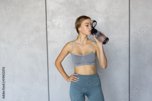 Woman drinking water at the home. Muscular woman taking break after exercise. Smiling attractive fitness woman after training. Jogger run runner energy sweaty yoga vitality wellness concept © dianagrytsku