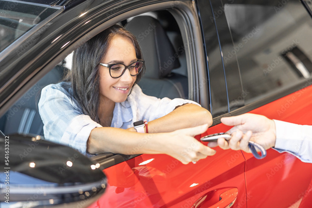 Happy woman receiving the keys of her new red car from the seller Happy woman receiving the keys of her new red car from the seller