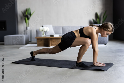 Sporty woman is doing working out at home and doing exercises in front of her laptop, wearing sport outfit