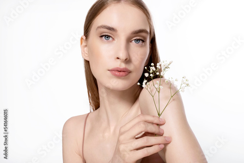 Cosmetic portrait of a young woman with perfect clean soft skin showing a flower as a symbol of ecological and natural cosmetics