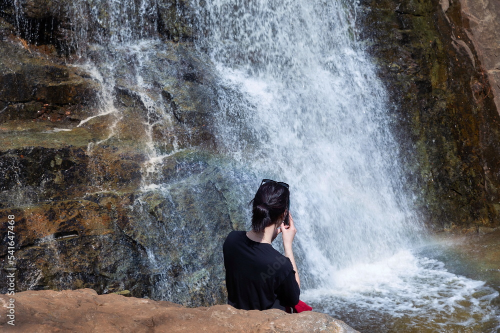 Obraz premium a tourist girl sits on a rock or admires Gadelsha, the largest waterfall in the Southern Urals, on a spring sunny day on the Irendyk ridge.