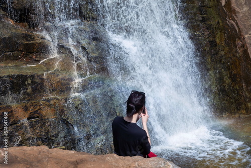 a tourist girl sits on a rock or admires Gadelsha  the largest waterfall in the Southern Urals  on a spring sunny day on the Irendyk ridge.