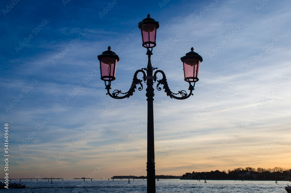 Un tipico lampione di Venezia si staglia sul tramonto con un cielo con delle belle nuvole