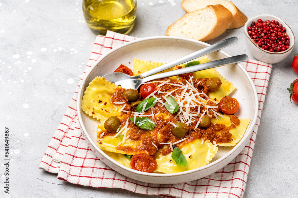 Italian food pasta ravioli with tomato sauce and olives with basil and cheese on a gray background. Italian food pasta ravioli with tomato sauce and olives with basil and cheese on a gray background.