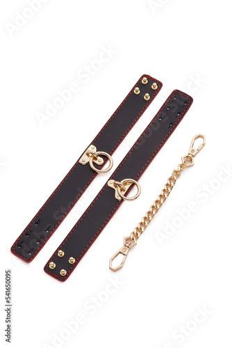Detailed shot of unbuckled black and red leather shackles with metal golden rivets and buckles. The fetters and a metal golden chain for them are isolated on the white background. photo