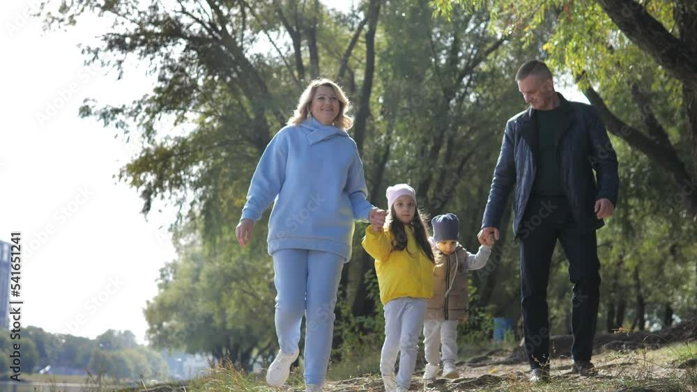 Young couple of grandparents with two little grandkids walking along river shore holding hands in autumn sunny day.Spend leisure time together outdoors for carefree lovely family happiness, recreation